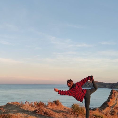 Frau praktiziert Yoga auf einem Fels, im Hintergrund Meer